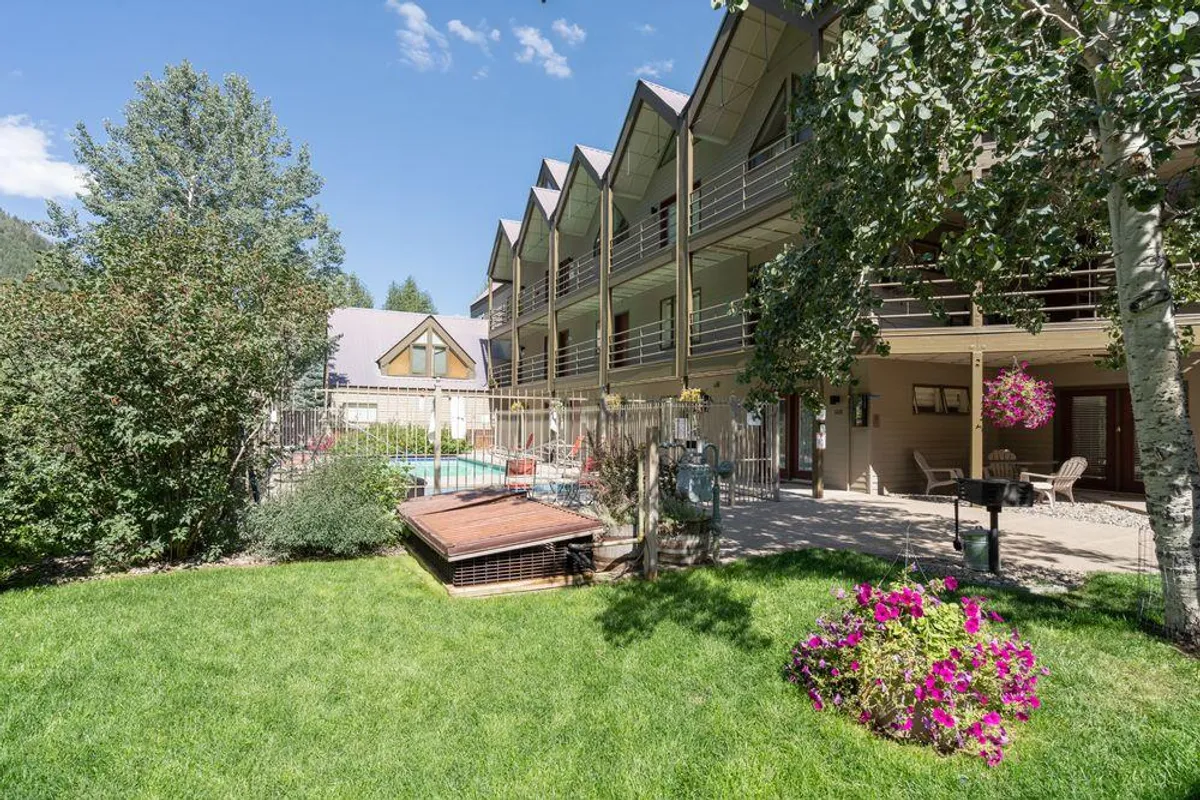 An exterior shot of the complex highlighting the swimming pool, landscaped gardens with flowers, and the building’s balconies. The scene is lively yet serene, inviting guests to visualize community amenities and seasonal relaxation.