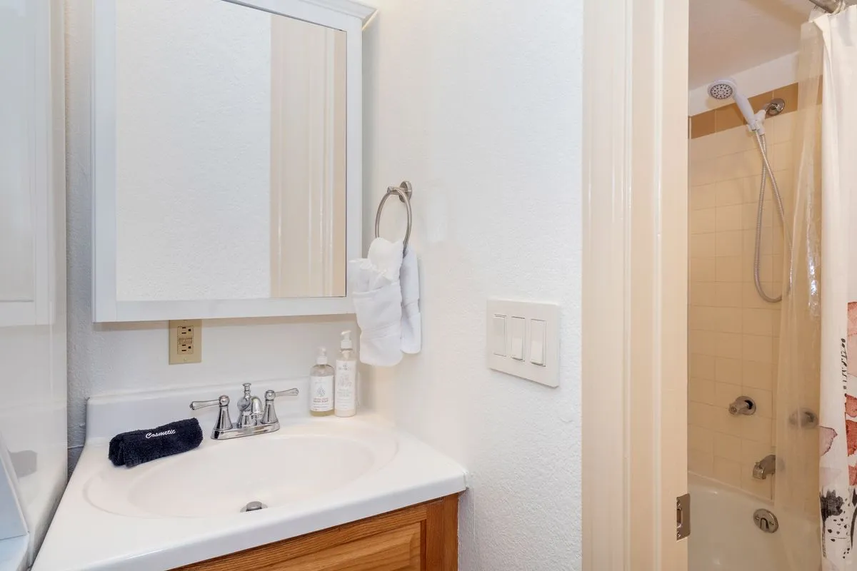 A close-up view of the bathroom featuring a sink, mirror, and shower area with neatly arranged towels. The space feels inviting and well-organized, ideal for personal grooming and relaxation.