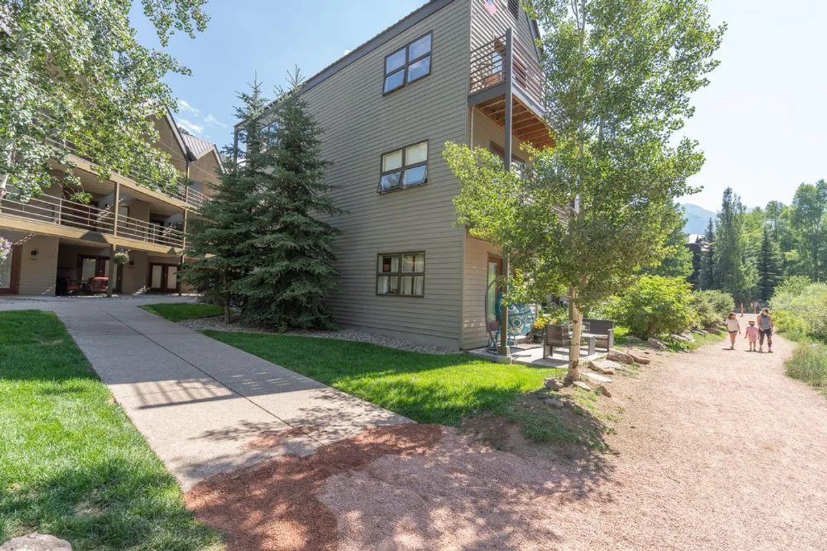 This exterior image features the building façade, a welcoming pathway, lush surrounding greenery, and people walking—suggesting easy access to outdoor spaces and the River Trail. The presence of people enjoying the outdoors captures the friendly, family-oriented atmosphere and highlights opportunities for exploration and gentle strolls.