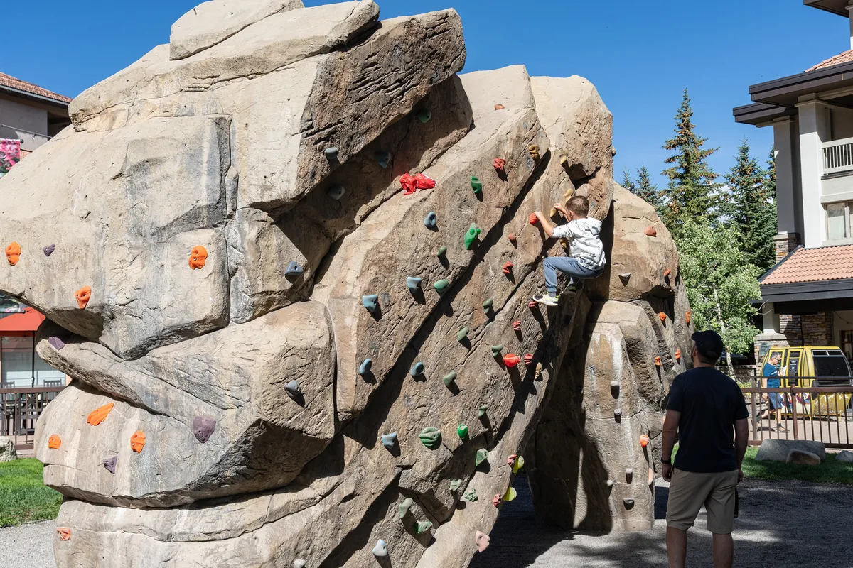 An exterior image of a child climbing a wall under the watchful eye of an adult, set in an energetic atmosphere. This highlights active outdoor play, family bonding, and the availability of kid-friendly activities in the area.
