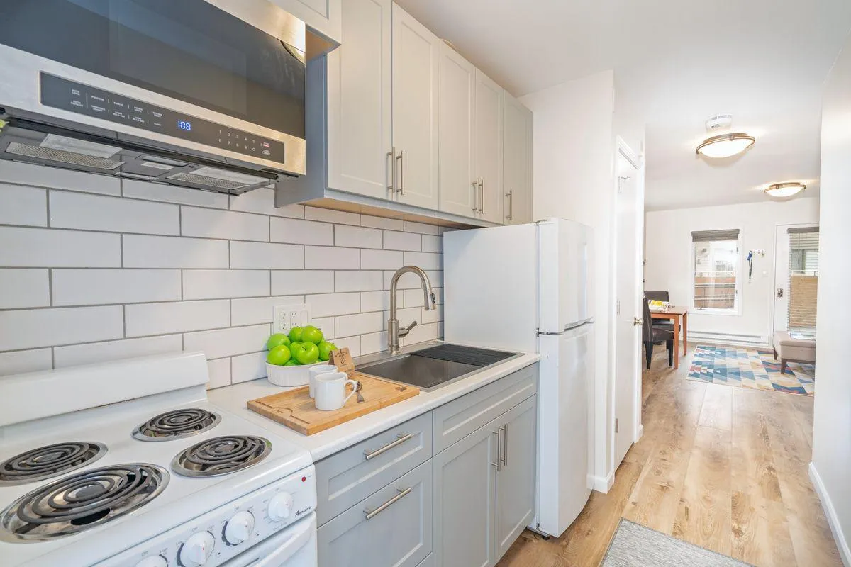 A modern kitchenette featuring stainless steel appliances, a white tiled backsplash, and a warm wooden countertop adorned with a bowl of fresh green apples. The space is bright and inviting, with everything needed for convenient meal preparation within easy reach.