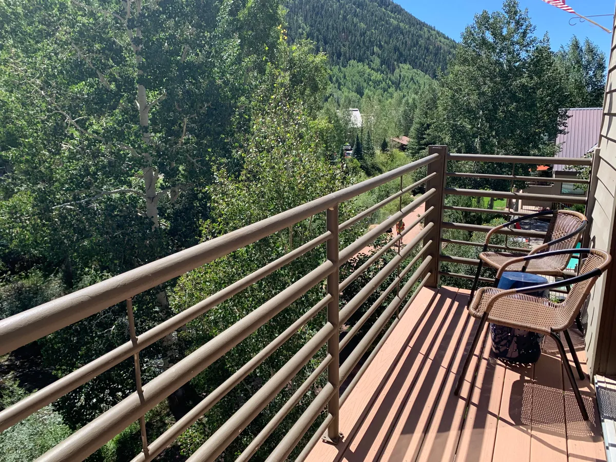 A private balcony with two chairs overlooks lush trees and a stunning mountain view. The balcony railing frames the scene, inviting you to enjoy a morning coffee or evening wine while taking in the tranquil sounds and sights of nature.